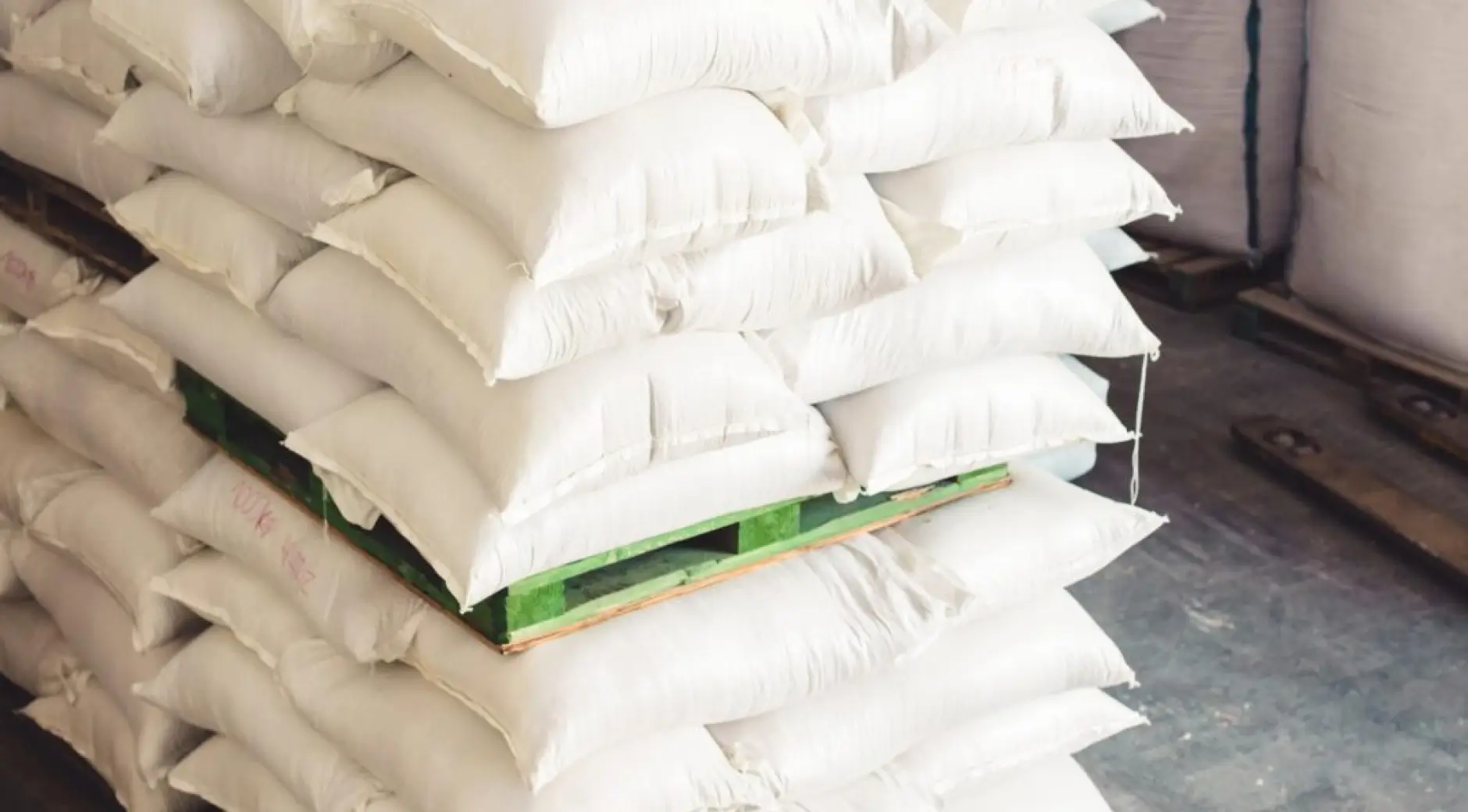 Close-up of stacked white polywoven sandbags showing double-stitched seams and construction durability with green pallet visible underneath.